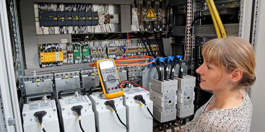 Junge Frau vor Schaltschrank in Elektromobilitätshalle Junge Frau vor Schaltschrank in Elektromobilitätshalle